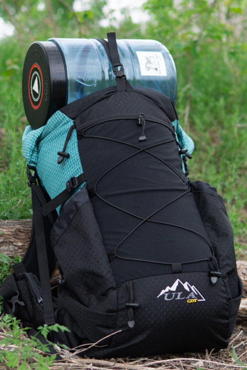 A hard sided bear can fits under the top strap of a ULA backpack for external carry