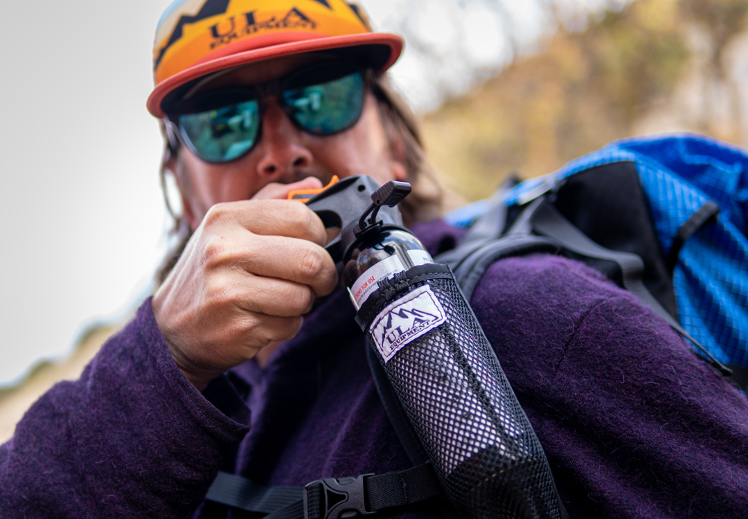 Backpacker reaches for his bear spray from the ULA Deploy Bear Canister Holder on his shoulder strap.