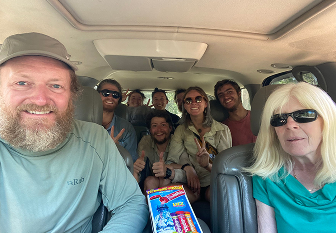 A group of hikers inside of a car are smiling with the driver.