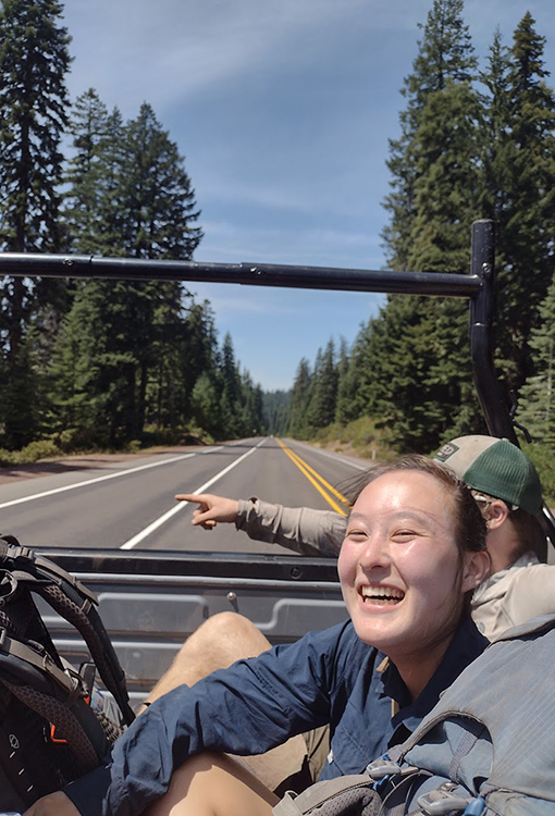 A woman smiles as she rides in the back of a pickup truck.