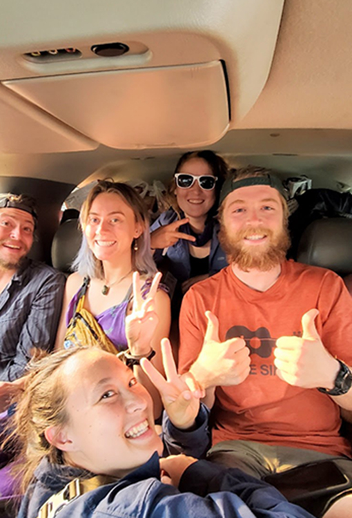 A group of people smile for the camera inside of a car.