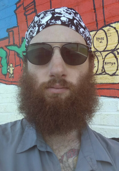 A bearded man wears a due rag and sunglasses.