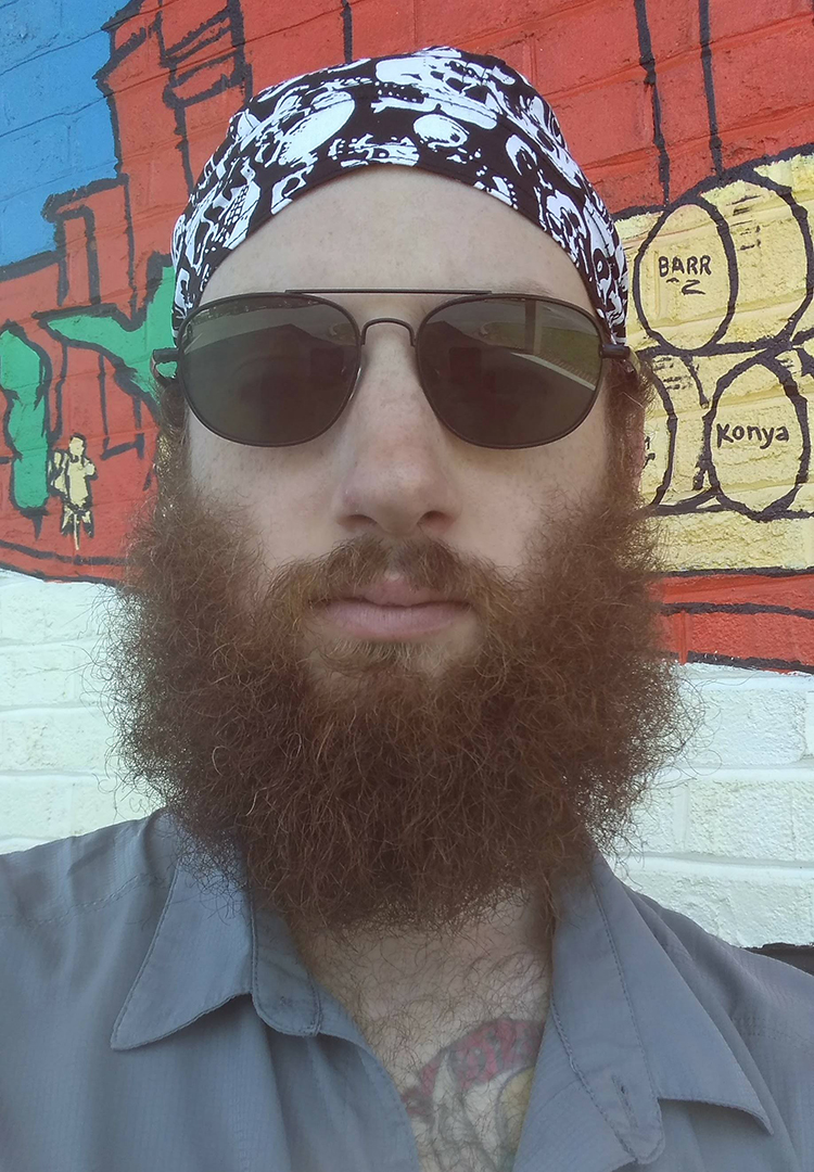 A bearded man wears a due rag and sunglasses.