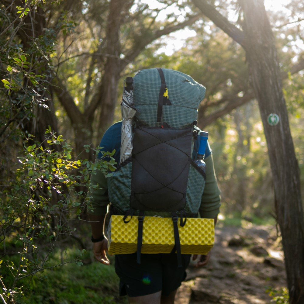 Backpacker on the trail with a ULA Circuit with Bottom Straps carrying a sleeping pad