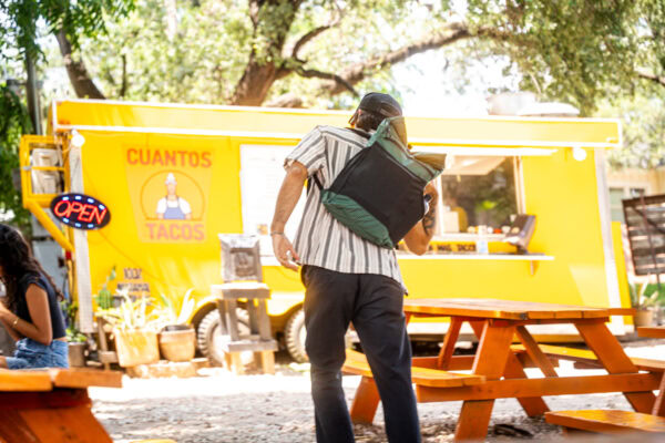 A person in front of a food truck removed their brushed green robic ULA node daypack