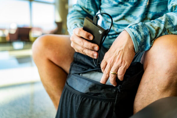A traveller in an airport inserts a battery charger into the front zipppered external pocket of a ULA Ultra Node