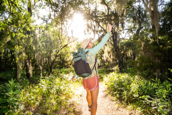 A female hiker wears a brushed green robic Node on the trail. It is summer and she is pointing at a tree.