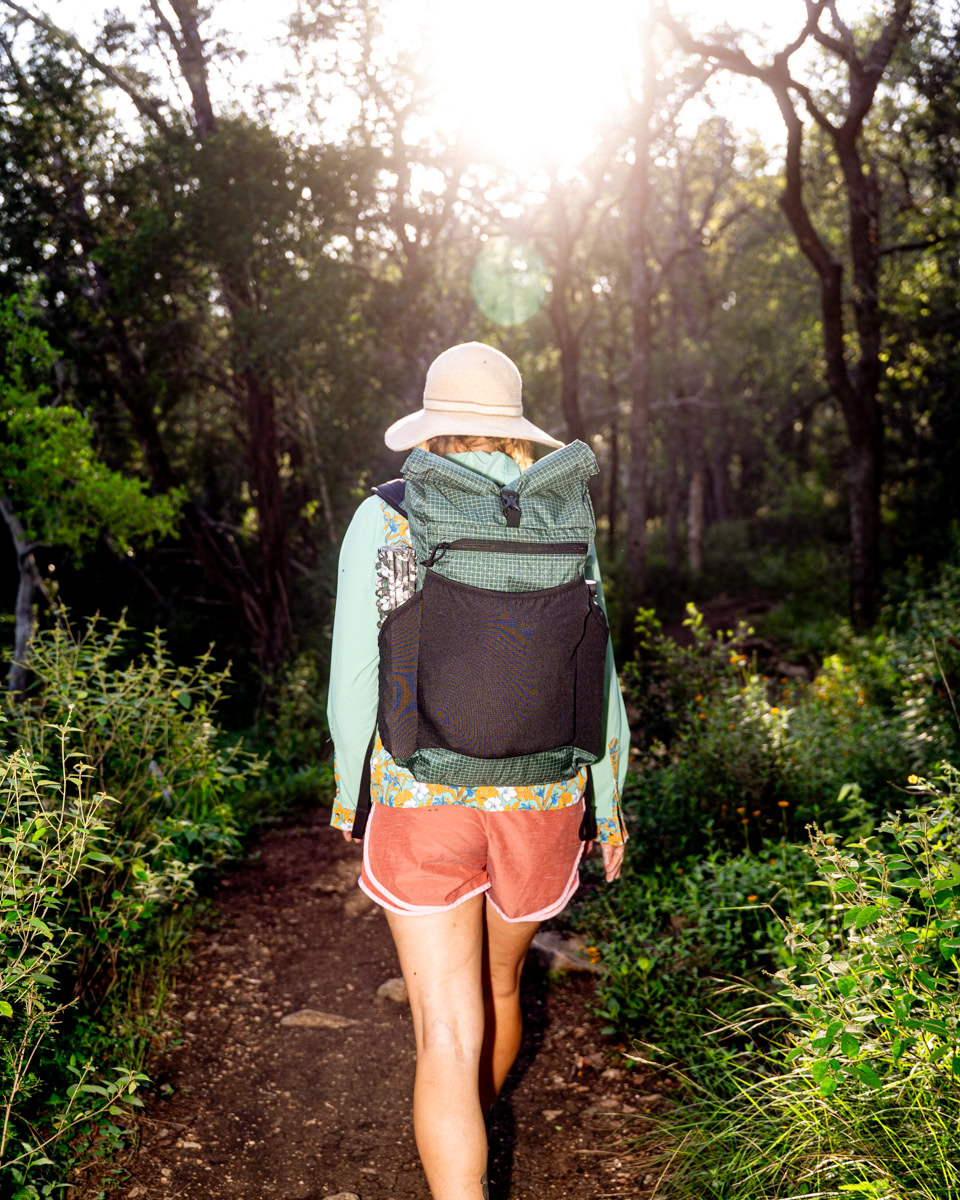 Green robic node outdoor-08 A woman walks outside with a sun hat and green backpack