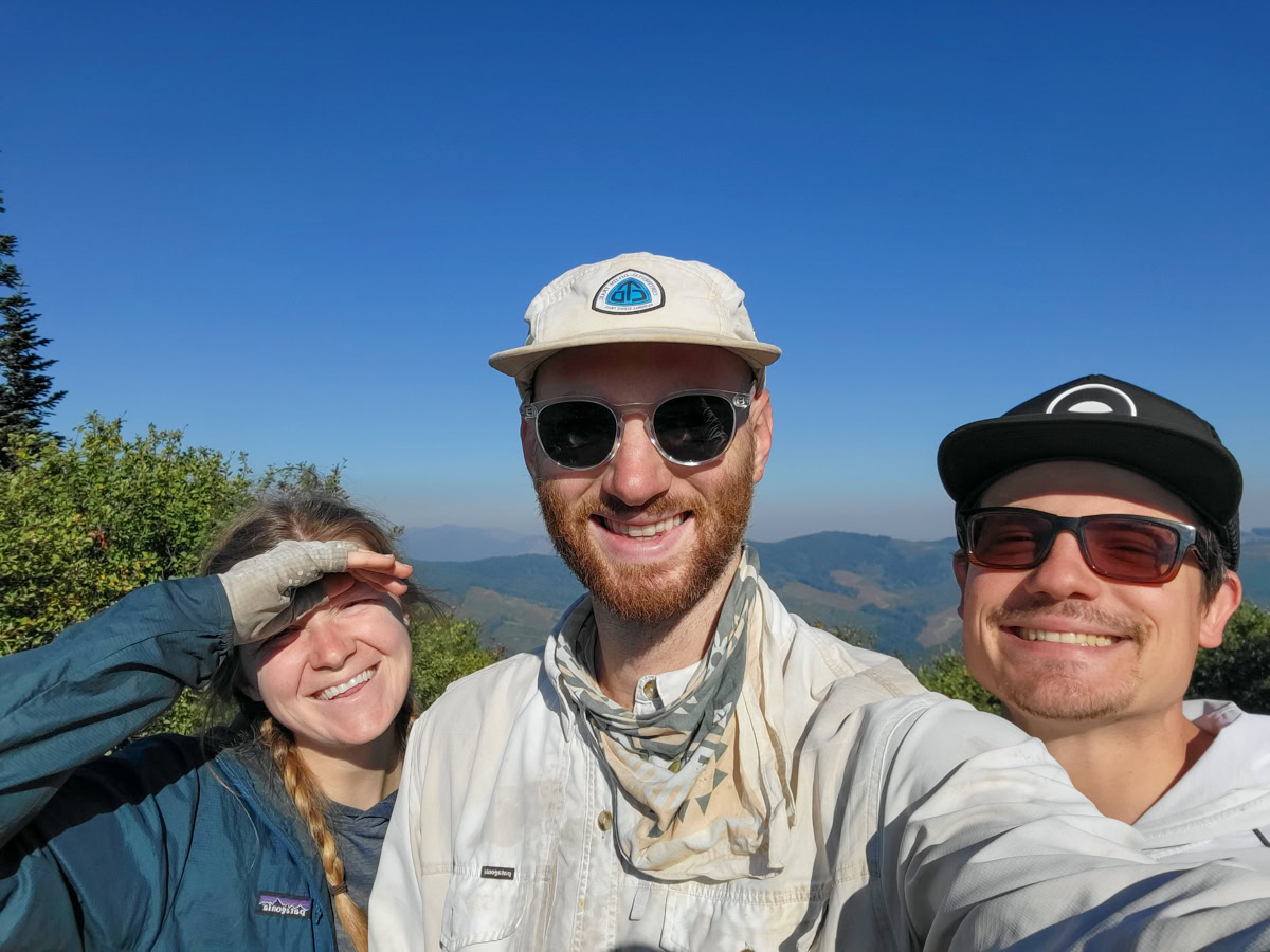 Hat, sunglasses, sun gloves, neck gaiter Two men and a woman smile into the camera