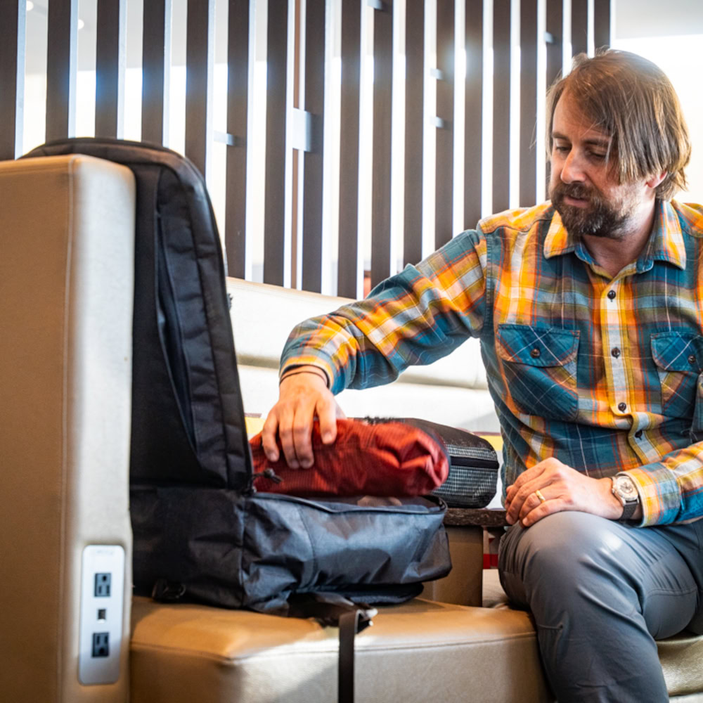 Urban traveler works on laptop in airport, with the ULA Ultra Node open next to him