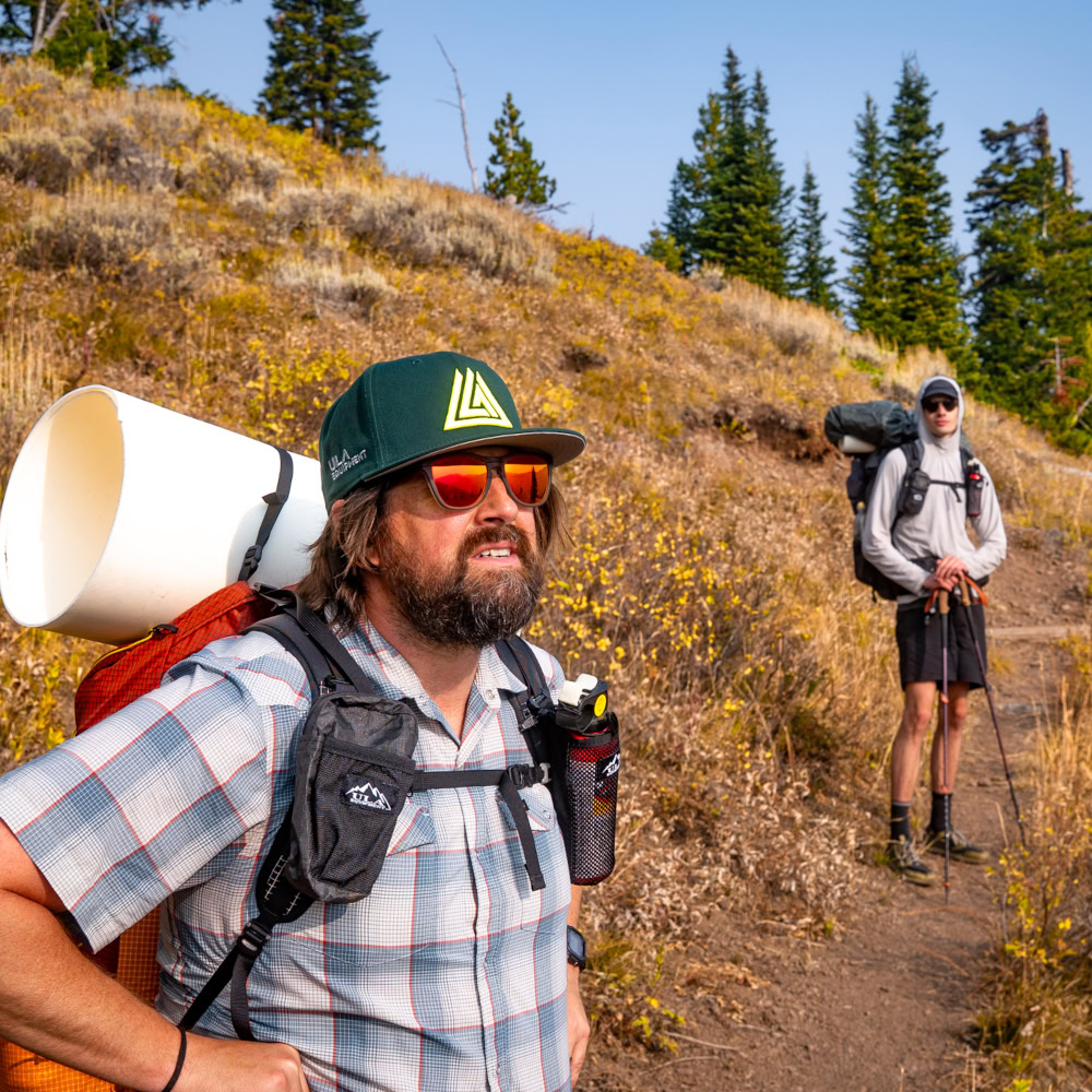 Tow backpackers stopped on a trail. The ULA Deploy is visible on the first packers strap.