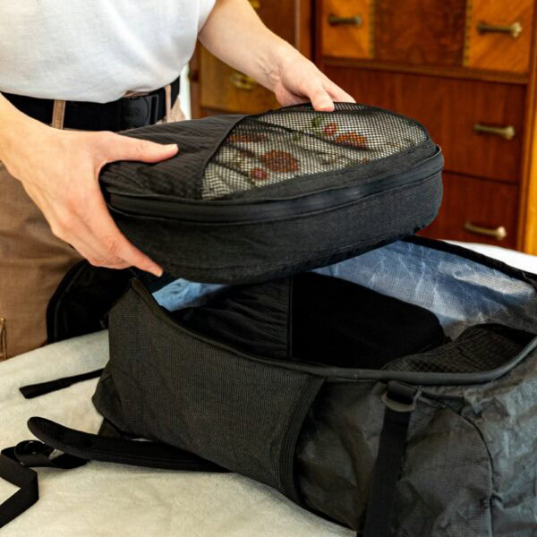 A traveller adds the packed conformist compression cube to their pack.