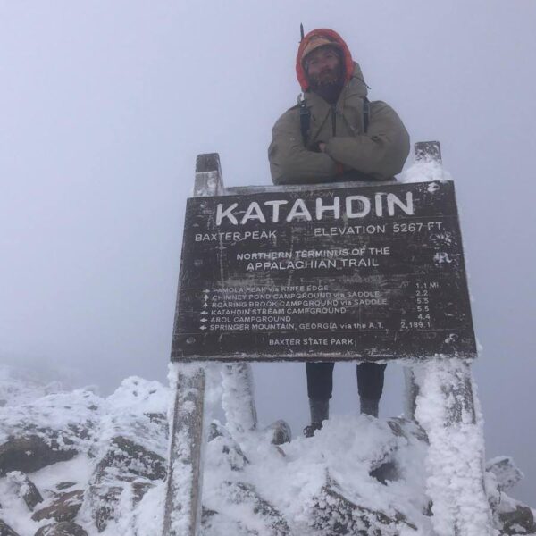A man stands at the Katahdin Sign