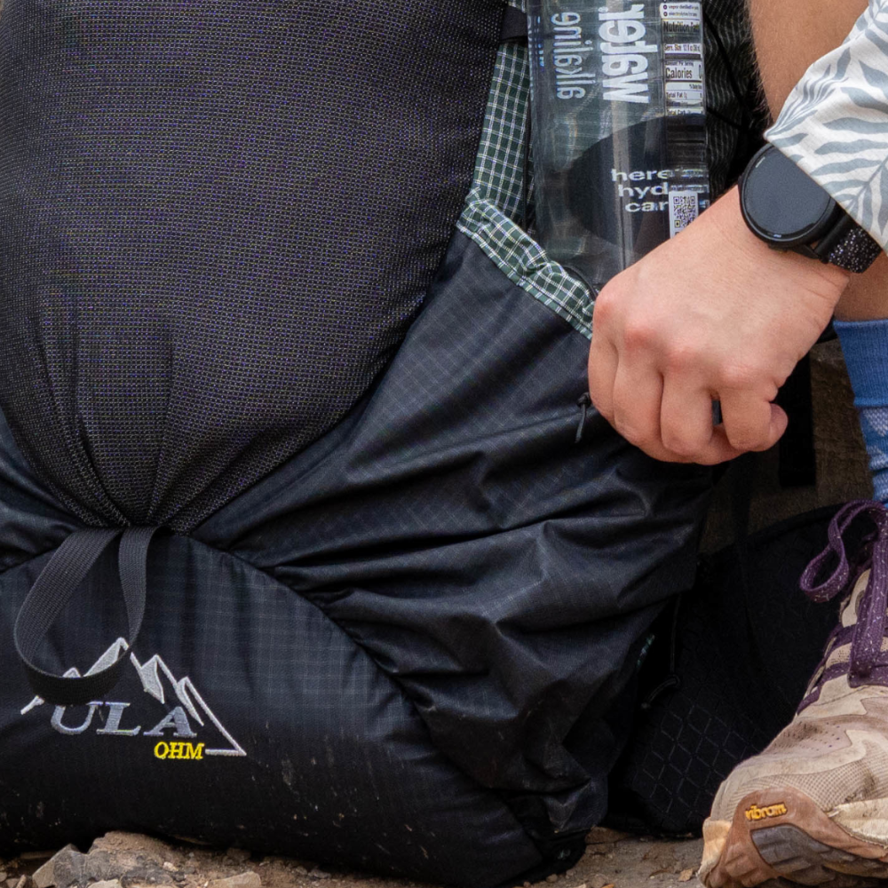 A hiker puts a water bottle in the side pocket on their 2026 UltraGrid ULA Ohm